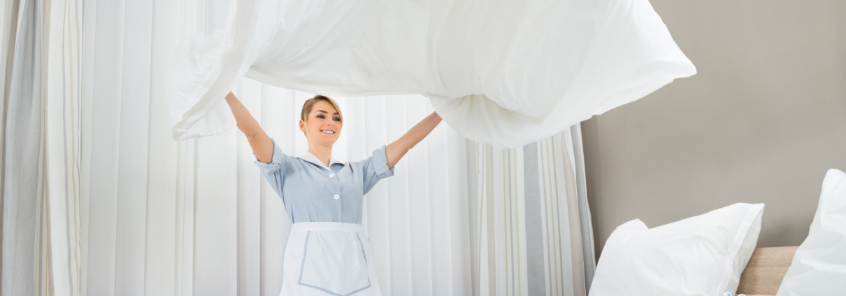happy female chambermaid making bed in hotel room