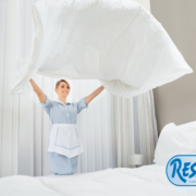 happy female chambermaid making bed in hotel room