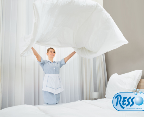 happy female chambermaid making bed in hotel room